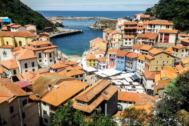 Vista del anfiteatro de casas de colores y tejados de teja roja de Cudillero, con el puerto y el Cantábrico al fondo